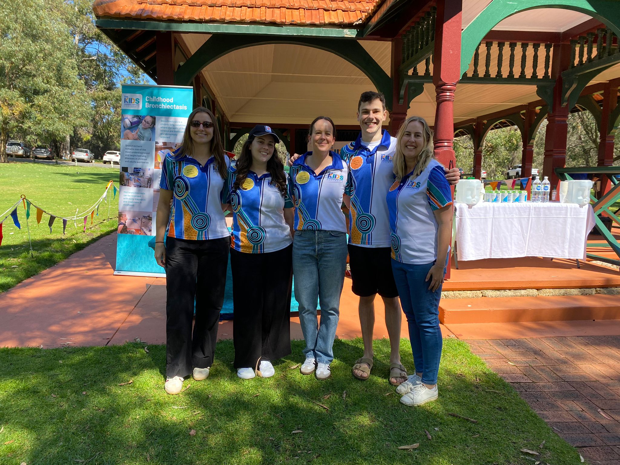 5 researchers in The Kids polo shirts standing in front of a gazebo, smiling