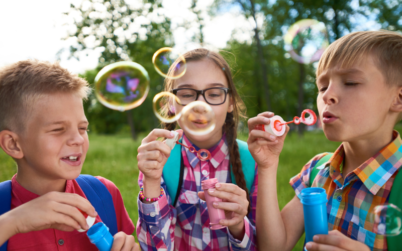 Three kids blowing bubbles in a park